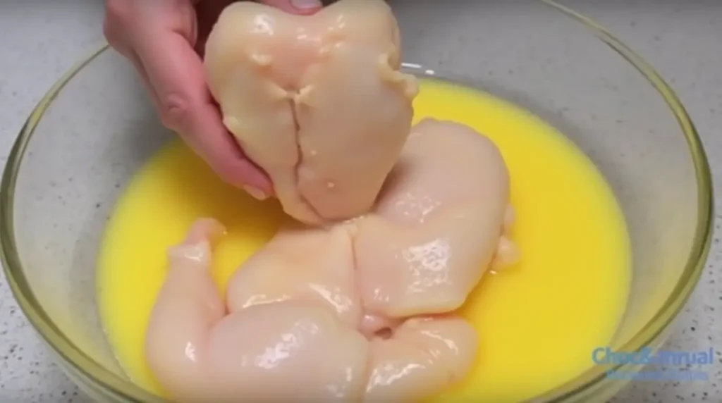 Image of chicken dipped into a bowl of beaten eggs, ready for breading