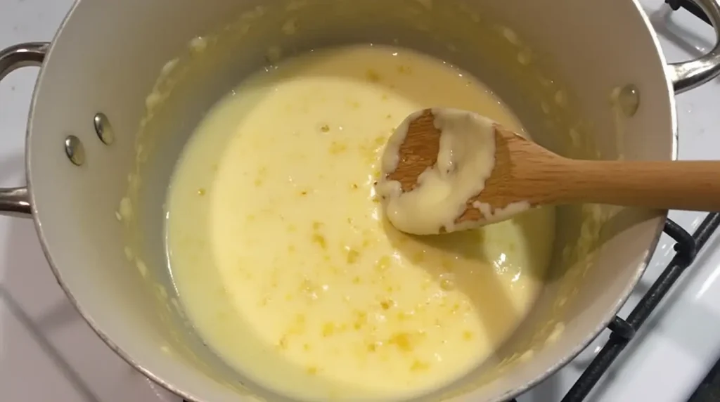 A saucepan with creamy parmesan sauce being stirred with a wooden spoon, with grated parmesan cheese melting into the mixture.