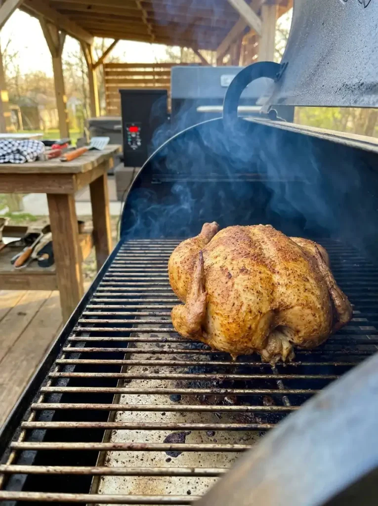 Smoked whole chicken cooking on a pellet grill with light smoke